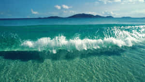 藍綠色海洋波浪帶著白色泡沫在清澈的淺水和遠處島嶼附近拍打。 — 海灘日落 壁紙