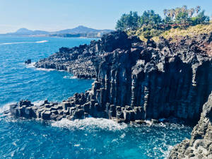 黑色玄武岩柱在明亮的陽光下從藍綠色海洋中升起。 — 제주도 壁紙
