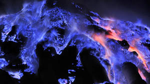 夜間在黑暗的火山岩上噴發的發光藍色和橙色熔岩流。 — 藍色火焰 壁紙