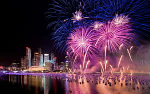五顏六色的煙火在夜間水面上反射的城市天際線上綻放。 — 新年快樂 壁紙