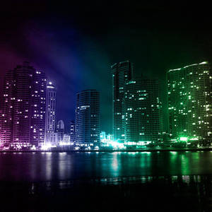 夜晚霓虹城市天際線倒映在水中，帶有紫色和綠色燈光。 — 城市燈光 壁紙