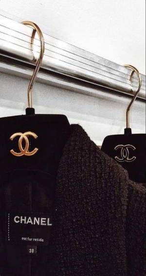 黑色 Chanel 服裝掛在金色衣架上，帶有可見的品牌標籤。 — 香奈兒標誌 壁紙