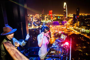 兩位DJ在屋頂上表演，俯瞰充滿活力的夜景城市景觀。 — 胡志明市 壁紙