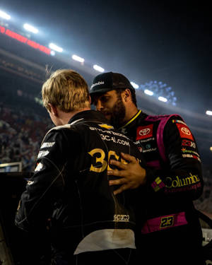 兩位NASCAR車手在體育場燈光下賽後擁抱，伴隨煙花。 — 4:5 壁紙