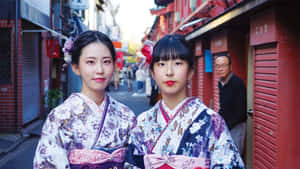 兩位年輕女性穿著色彩繽紛的和服，在狹窄的日本小巷中擺姿勢。 — 日本 壁紙