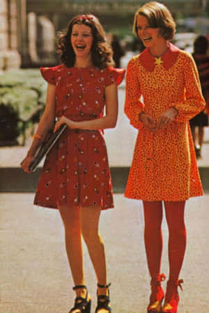 兩位穿著色彩繽紛1960年代連衣裙的女性笑著走在戶外。 — 70年代動圖 壁紙