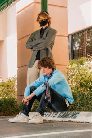 兩位穿著潮流服裝的年輕男子在建築物外的遊戲標誌附近擺姿勢。 — Tubbo 壁紙