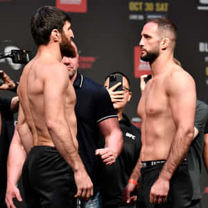 兩位赤裸上身的MMA拳手在UFC稱重活動中互相凝視，周圍有攝影師。 — 終極格鬥冠軍賽 壁紙