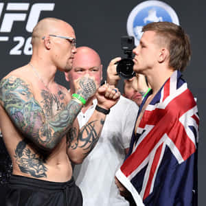 兩位男性UFC拳手在比賽前互相凝視，一人有刺青，另一人披著英國國旗。 — 終極格鬥冠軍賽 壁紙