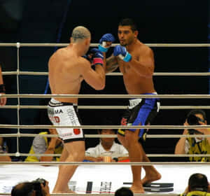兩位MMA拳手在擂台上互相出拳，攝影師在旁觀看。 — 運動 壁紙