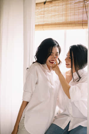 兩位女性在有竹簾的窗邊一起笑。 — 女同志 GIF 壁紙