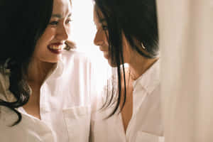 兩位身穿白襯衫的女性在柔和光線中溫暖地微笑相對。 — 女同志 GIF 壁紙