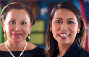 兩位穿著職業裝的女性在室內對著鏡頭微笑。 — 紐約 壁紙