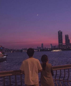 兩個人在暮色中觀看新月在城市天際線之上。 — 美學愛情 壁紙