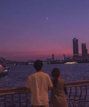 兩個人在暮色中觀看城市天際線上的月亮。 — 美學天空 壁紙