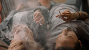 兩個人躺著吸煙，煙霧環繞他們的臉龐。 — 抽菸 壁紙