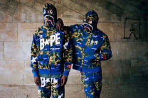 兩位模特兒在城市石隧道中穿著Bape鯊魚迷彩連帽衫和褲子。 — Bape 動態 壁紙