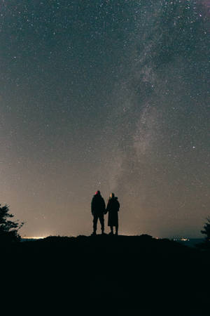 兩個人手牽手，在星空下凝視著銀河。 — 夜晚 壁紙