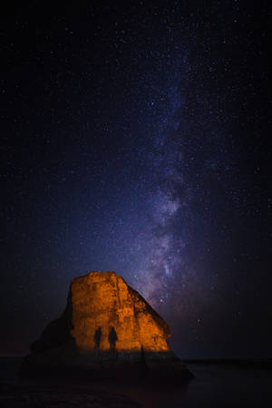 兩人在星空下站在發光的岩石上，銀河可見。 — 鯊魚 壁紙