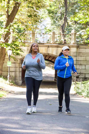 兩個女人在公園的鋪砌小徑上慢跑，背景是一座石橋。 — Running 壁紙