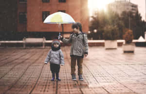 兩個孩子在磚砌廣場上撐著雨傘在雨中行走。 — 後代 壁紙