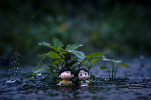 兩個小公仔在降雨期間坐在水中，附近有植物。 — 娃娃 壁紙