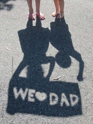 小孩的影子在人行道上用粉筆拼出「WE ❤️ DAD」。 — 父親節 壁紙