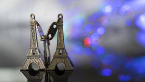 兩個刻有「Paris」的小型艾菲爾鐵塔鑰匙圈，掛在模糊的藍色燈光背景上。 — 艾菲爾鐵塔 壁紙