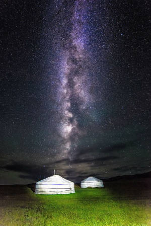 在充滿活力的銀河星空下，兩個發光的蒙古包。 — 寬扎節 壁紙