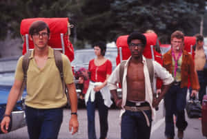 兩個背著紅色背包的男人在汽車和樹木的道路上行走。 — Woodstock 壁紙