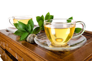 兩個玻璃茶杯放在一個有綠葉和茶球的木托盤上。 — 茶園 壁紙