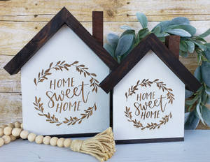 兩個房屋形狀的木製標牌，上面寫著「Home Sweet Home」，帶有樹葉花環和質樸裝飾。 — 甜蜜的家 壁紙