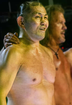 兩個汗流浹背的男人在溫暖的舞台燈光下微笑，其中一個把手放在肩膀上。 — 摔角 壁紙