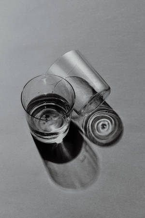 兩個玻璃杯，一個直立，一個傾倒，在灰色表面上投射陰影 — 酷 壁紙