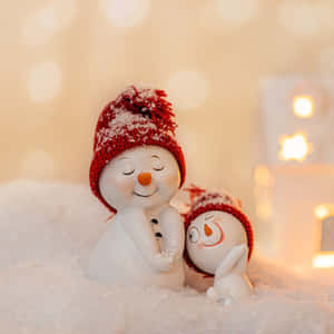 兩個雪人公仔在雪中擁抱，身後有溫暖的燈光。 — 美麗聖誕 壁紙