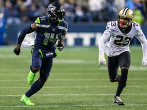 兩名足球運動員在比賽期間在綠色場地上奔跑。 — Dk Metcalf 壁紙