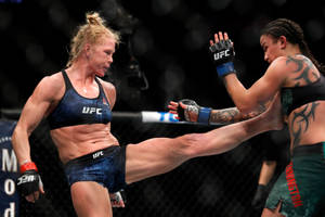 籠中的兩名女性MMA拳手，一人踢向另一人，後者阻擋。 — 終極格鬥冠軍賽 壁紙