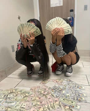 兩名女孩蹲在走廊上，用扇形的美元鈔票遮住臉，地上有現金。 — 可愛壞女孩 壁紙