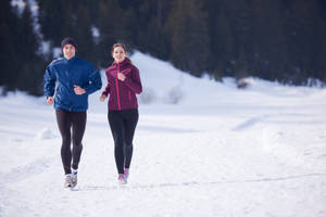 兩人在雪覆蓋的樹林中穿著冬季跑步裝備慢跑。 — 冬季 壁紙