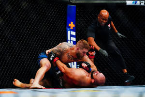 兩名MMA拳手在UFC八角籠內纏鬥，裁判在旁觀看。 — 終極格鬥冠軍賽 壁紙