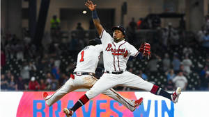 兩名棒球運動員在夜間比賽中跳躍慶祝，帶有「BRAVES WIN」標誌。 — 小羅納德·阿庫尼亞 壁紙