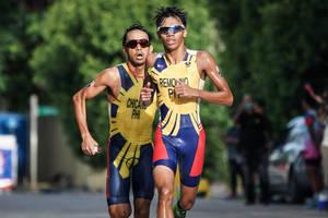 兩名男性鐵人三項運動員身穿黃、藍、紅色制服在街上比賽。 — 運動 壁紙