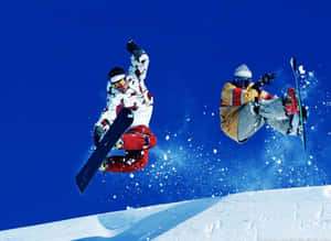 兩名滑雪板運動員在晴朗的藍天下，在白雪覆蓋的山坡上表演空中技巧。 — 酷寒冬季 壁紙