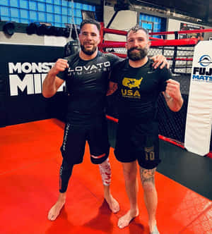 兩名男性MMA拳手在鋪有紅色軟墊及品牌牆壁的健身房內擺姿勢。 — 運動 壁紙