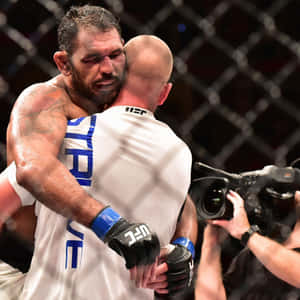 兩名男性MMA拳手在UFC比賽後於八角籠內擁抱。 — 終極格鬥冠軍賽 壁紙