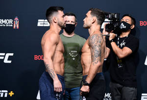 兩名赤裸上身的MMA拳手在UFC稱重儀式上互相凝視，周圍有相機。 — 終極格鬥冠軍賽 壁紙
