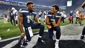兩名海鷹隊球員晚上在美式足球場上跪著交談。 — Dk Metcalf 壁紙