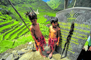 兩名身穿傳統服飾的年輕原住民男孩站在標誌附近，俯瞰梯田。 — 菲律賓 壁紙