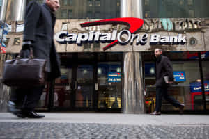 兩名商人走過一間設有玻璃門和24小時自動櫃員機標誌的Capital One銀行。 — 人物 壁紙