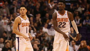 兩名鳳凰城太陽隊籃球運動員在比賽中站在球場上，背景有觀眾。 — Devin Booker 壁紙
